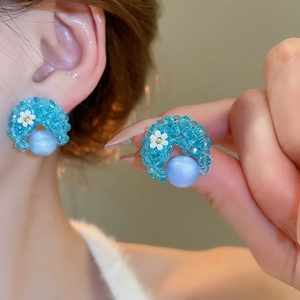 Detail view of blue faceted crystal earrings with flower accent and light blue pearl.
