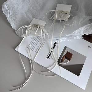 Detailed view of handmade bow hair clips with white silk ribbons and silver beads on a magazine