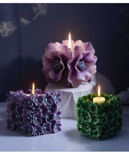 Vista detallada de velas aromáticas encendidas con formas florales moradas y verde oscuro