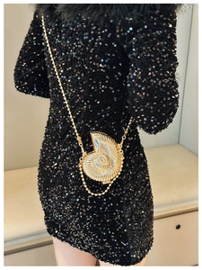 Detailed view of a gold shell-shaped clutch bag paired with a black sequin dress