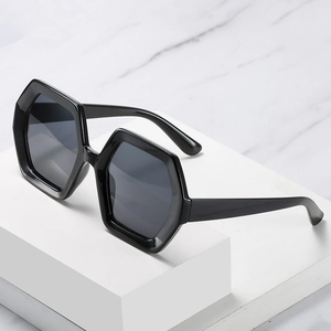 Modern black oversized hexagonal sunglasses on a marble background in a 45-degree angle view
