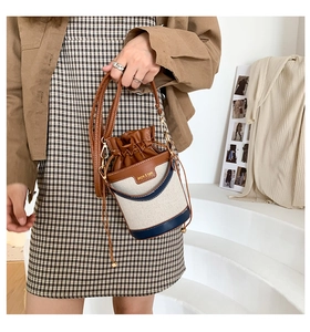 Detail of canvas bucket bag with leather trim and drawstring closure held by a model