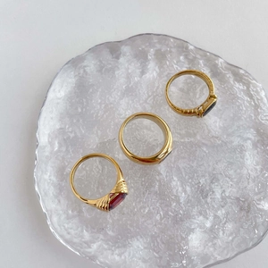 Macro view of gold-plated rings with black and ruby stones on a textured glass tray