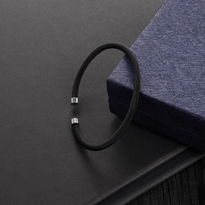 Close-up of black mesh woven bracelet with silver cylindrical metal ends on a dark box