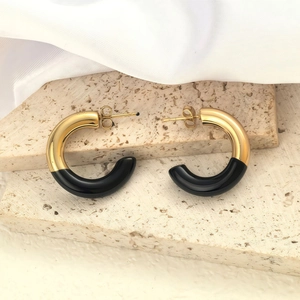 Detail of C-shaped hoop earrings featuring gold polished metal and black glossy resin