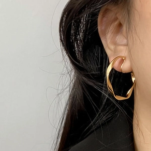 Close-up of a model wearing a gold irregular twisted cuff earring with a minimalist finish