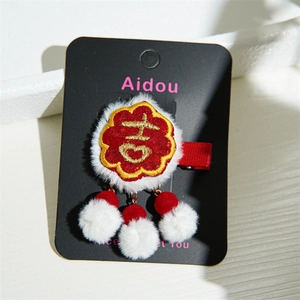 Close-up of red festive plush hair clip with gold Ji embroidery and white faux fur trim