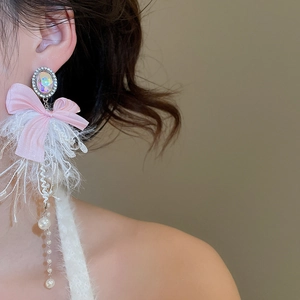 Close-up of long bow earrings with pink ribbons, feathers and pearls on a model