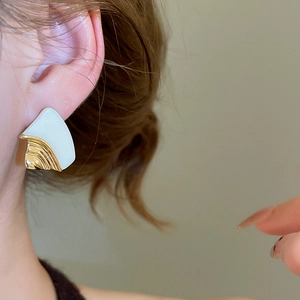 Close-up of 18k gold plated geometric earrings with white resin inlay on a female ear