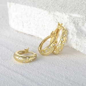 Macro shot of gold star-patterned hoop earrings with small crystals on white stone