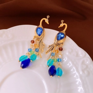 Detail of peacock earrings with blue gemstones and colorful beaded tassels on ceramic
