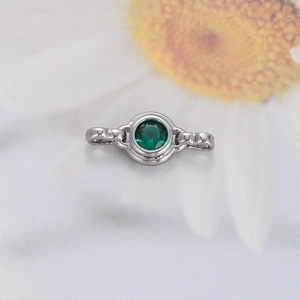 Close-up of silver jewelry connector with round green zircon on floral fabric background