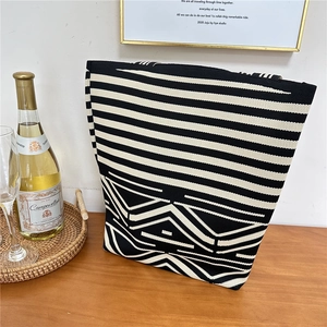 Detail of a black and white knit tote bag with geometric patterns on a wooden table