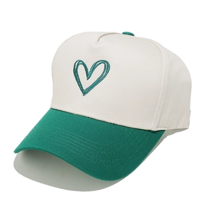 Detail of green heart embroidery on a white and green colorblock cotton baseball cap