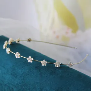Dettaglio del sottile cerchietto in lega dorata con sette fiori di resina bianca e piccoli strass