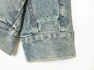 Detail of light blue denim sleeve cuff showing washed texture and stitching on cotton jacket