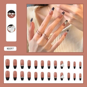 Macro view of coffin shaped press-on nails in pink with black French tips and heart charms