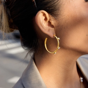 Detail of gold-plated stainless steel hoop earrings with three inset zircon stones