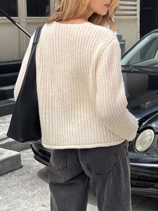 Détail d'un pull en maille épaisse crème à coupe ample et col rond dans une rue urbaine