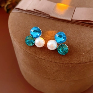 Macro shot of triangle crystal pearl earrings on brown velvet jewelry box with warm lighting