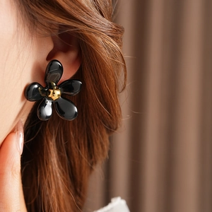Close-up of a stylish black floral earring with golden center worn by a female model