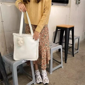 Detail of white tote bag featuring plush faux fur trim and cute bear charm in a cafe setting
