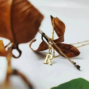 Detailed view of a gold titanium steel letter R pendant necklace on a dainty bead chain