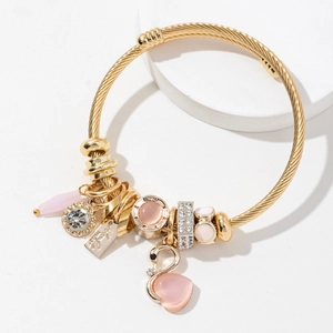 Golden woven bracelet with pink swan, cat-eye stone, and crystal charms on white stand