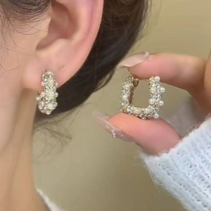 Close-up of gold-plated U-shaped earrings featuring white pearls and tiny crystals