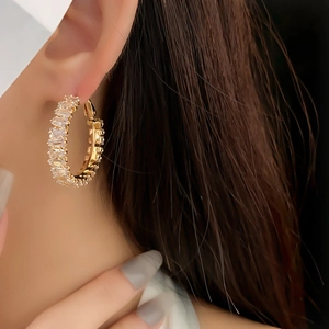 Close-up of gold hoop earrings with sparkling square cut zircons worn by a model