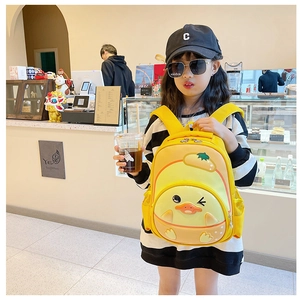 Toddler girl wearing a yellow cartoon duck backpack in a cafe setting outdoors