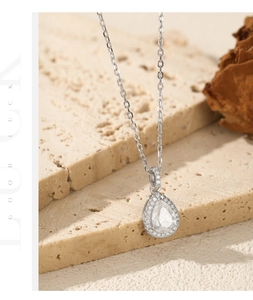 Macro detail of silver pear cut teardrop pendant necklace on beige stone background