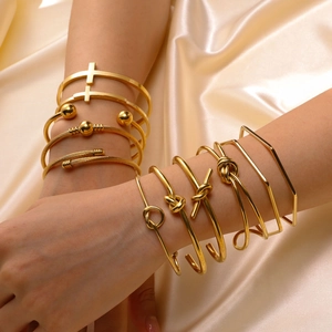 Stack of gold knot and geometric C-shaped open bracelets on a silk background