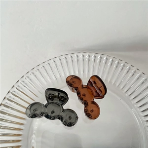 Close-up of translucent grey and amber mini hair claws on a glass tray in a minimalist setting