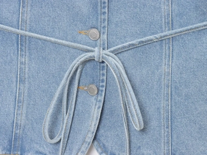 Vue détaillée du gilet en jean avec boutons métalliques et cordon en bleu clair