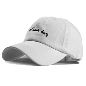 Close-up of black 'bad hair day' embroidery on a white cotton baseball cap surface