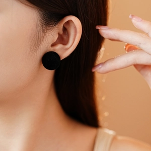 Close-up of a minimalist black flocked circular stud earring worn by a model