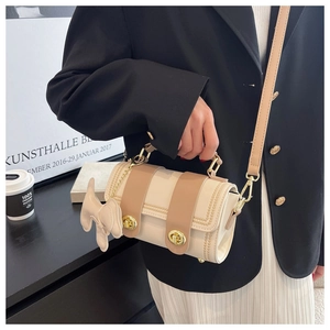 Dettaglio di una mini borsa a tracolla beige e kaki con chiusure dorate su un blazer nero