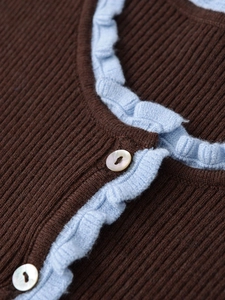 Detail of dark brown ribbed knit top with light blue ruffles and shell buttons