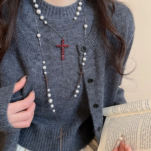Detail einer mehrlagigen Kreuzkette mit roten Strasssteinen und weißen Perlen auf Pullover