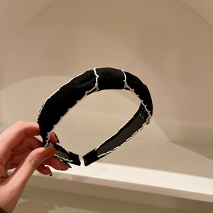 Close-up of black fabric headband featuring white contrast hand-stitched decorative edges