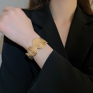 Detail of a wide gold cuff bracelet featuring textured spiral disks worn on a black blazer