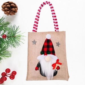 Christmas burlap gift bag with gnome pattern and red striped handles on white wood