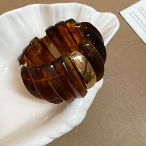 Détail d'un large bracelet en résine ambrée et métal doré dans un plateau coquille