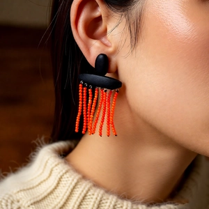 Close-up of ethnic orange beaded fringe earrings with black base on a model