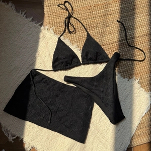 Detailed view of black textured three-piece bikini with halter top and lace-up skirt