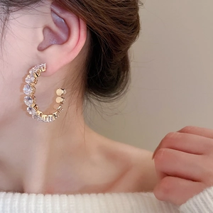 Close-up of elegant C-shaped gold earrings with sparkling rhinestones on a female model