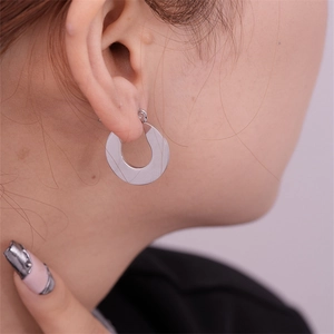 Close-up of a minimalist silver-tone flat hoop earring worn on a model's ear lobe