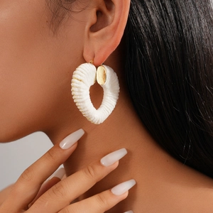 Close-up of white woven heart hoop earrings with gold bead trim on a model