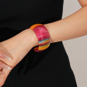 Detail of a wide colorful striped acetate open bangle on a model's wrist against black fabric